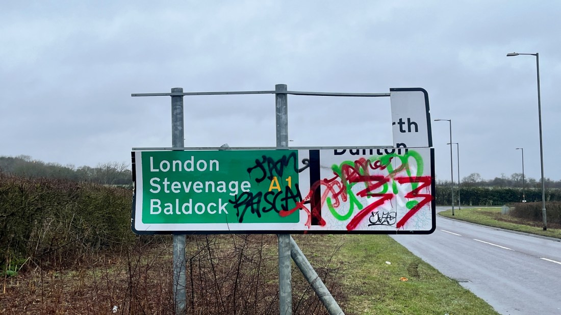 A broken road sign covered in graffiti.