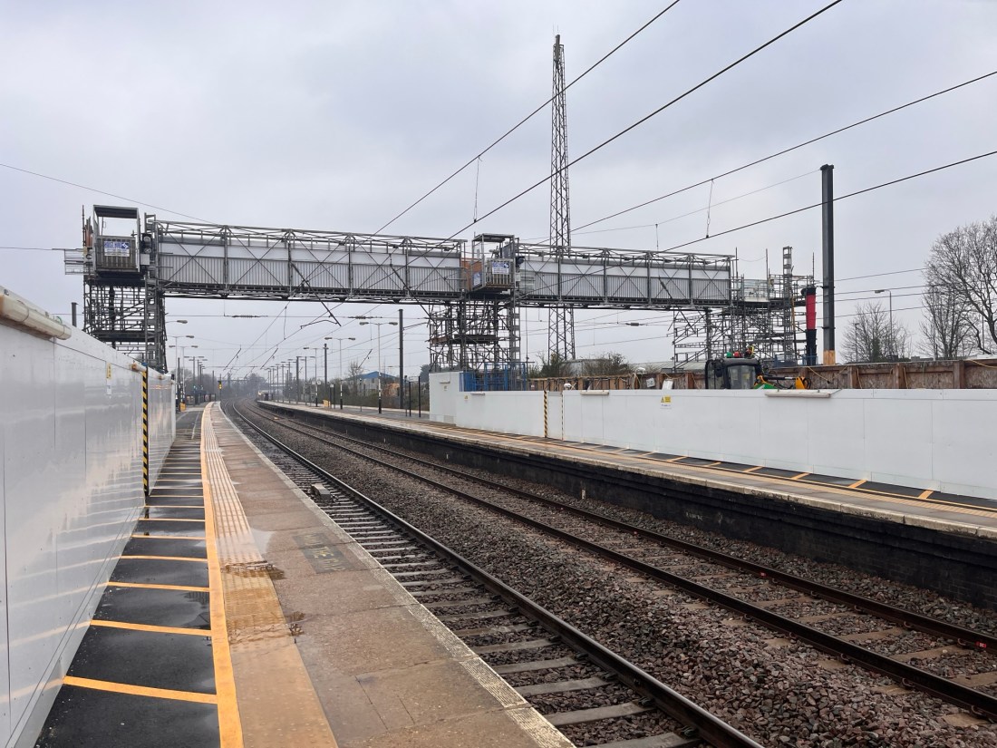 A scaffold bridge over the railway lines at Biggleswade station on a cloudy day.