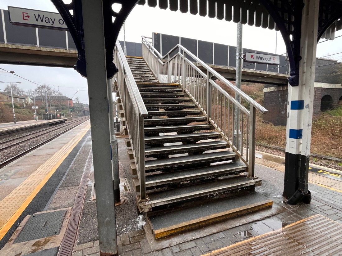 A set of steps leading down to a railway platform on a grey day.