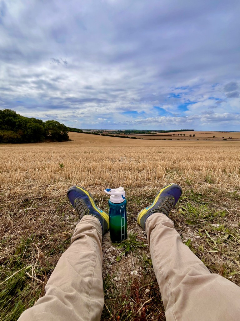A pair of legs and a drink bottle with a backdrop of a harvested field.