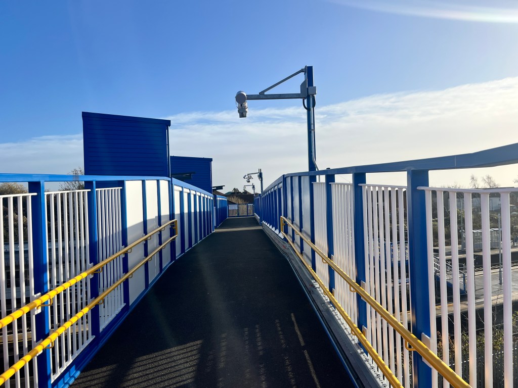 The new bridge at Biggleswade with blue railings a yellow handrails under a blue sky.